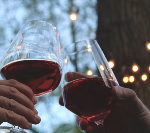 Zwei Personen stoßen mit Weingläsern an. Sie verkosten die "la traversara" Weine vom Weingut Wieserhof in Völlan, Südtirol.